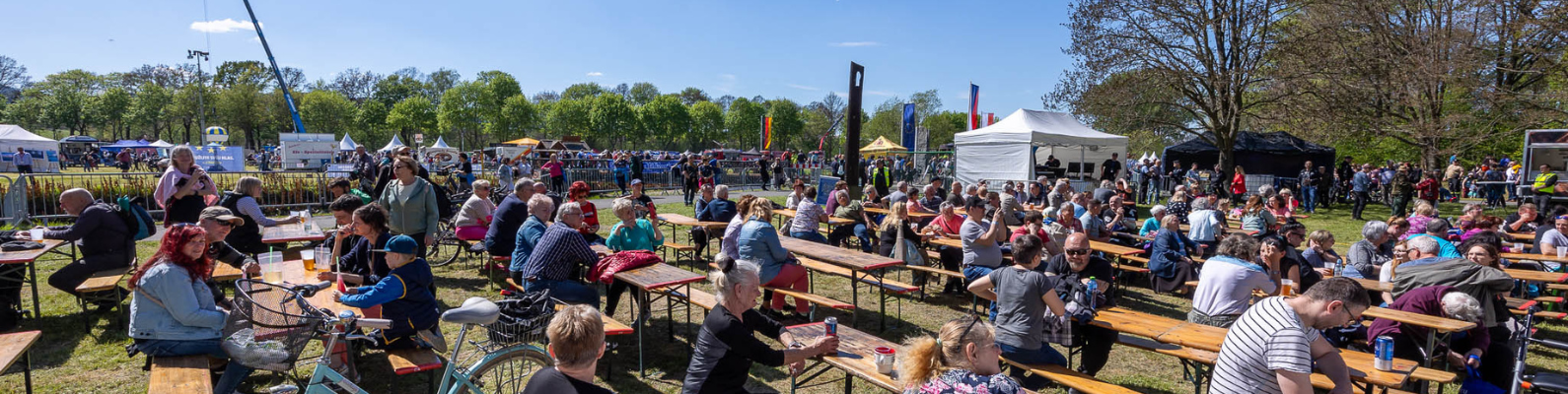 Ein Bild von vielen Menschen, die auf dem Europafest auf Bierbänken in der Sonne sitzen.