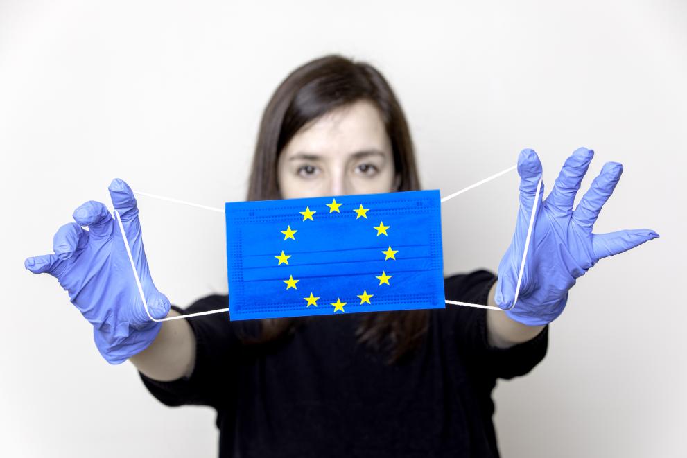 Young woman wearing gloves and holding a face mask with the European symbol.