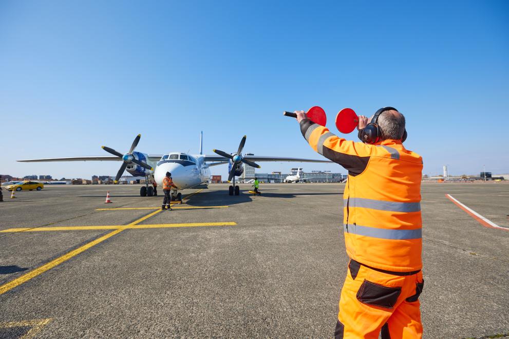 An air traffic controller shows an aircraft on the runway two red signs to stop.