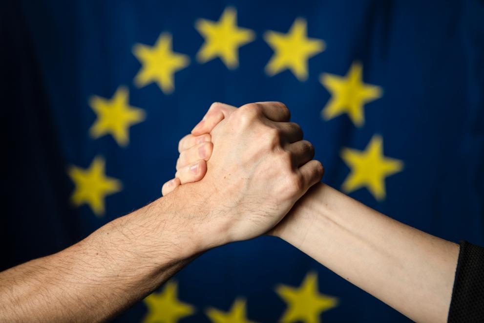 Two hands shaking infront of the EU flag.