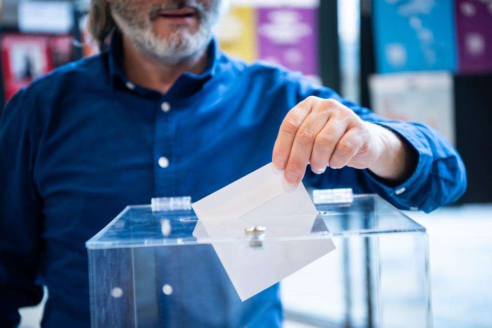 A man voting by putting a letter into a transparent plastic box.