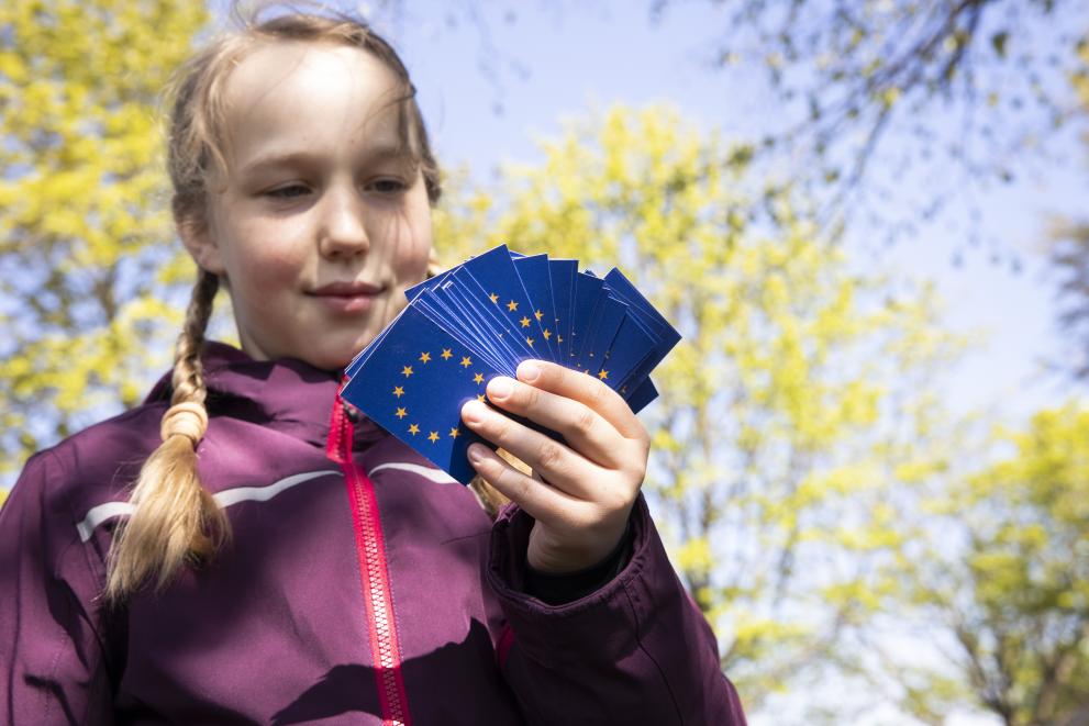 A girl standing outside and holding a dozen of cards with the EU flag on it in her hands.