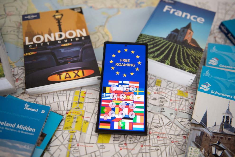 A smartphone with the text "free roaming" laying on a road map and is surrounded by travel books.