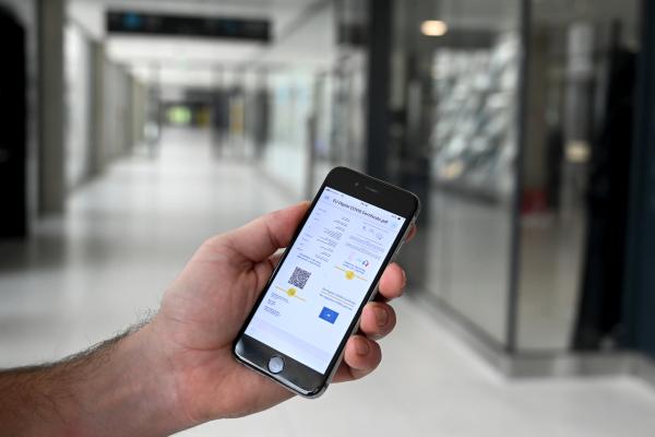 A hand holding a smartphone with the CovPass App opened on it.